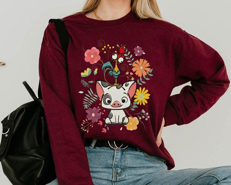 Pu&ograve; includere: Felpa color borgogna con un design di un maiale e un gallo di cartone animato. Il maiale indossa una corona di fiori e il gallo &egrave; in piedi sulla testa del maiale. Il design &egrave; circondato da fiori e foglie.