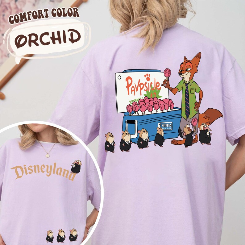 Puede incluir: Una camiseta de color lila claro con la palabra "Disneyland" en escritura dorada en la parte delantera. La parte trasera presenta un zorro de dibujos animados vendiendo paletas de un refrigerador, con el texto "Pavpsicle". La camiseta est&aacute; etiquetada como "Comfort Color Orchid".