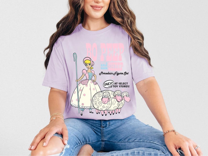 May include: A purple t-shirt with a graphic of Bo Peep and her sheep from the Toy Story movie. The text on the shirt reads "Bo Peep and her sheep Porcelain Figure Set Only at Select Toy Stores!"