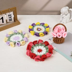 May include: A collection of handmade crochet flowers and a basket of flowers. The flowers are in various colors, including red, pink, yellow, purple, and white. The basket is brown and filled with pink flowers. A wooden calendar shows the date as March 1.