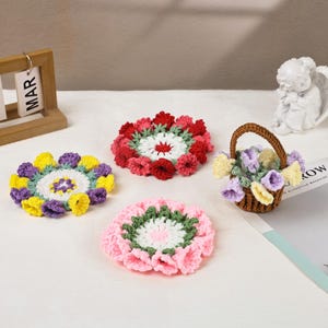 Könnte beinhalten: Eine Sammlung handgefertigter gehäkelter Blumenuntersetzer in verschiedenen Farben, darunter Gelb, Lila, Rot und Rosa. Ein kleiner brauner Korb mit gehäkelten Blumen ist ebenfalls vorhanden. Die Untersetzer sind auf einer weißen Oberfläche angeordnet.