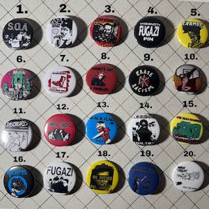 May include: Twenty colorful button pins featuring various punk rock bands, including SOA, Black Flag, Minor Threat, Fugazi, and The Cramps. The pins are arranged in a grid pattern on a white background.