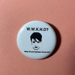 Pu&ograve; includere: Bottone bianco con testo nero e un'illustrazione in bianco e nero del viso di una donna. Il testo dice "W.W.K.H.D? What Would Kathleen Hanna Do?"