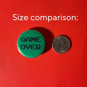 May include: Green button with the text "GAME OVER" in black pixelated letters. The button is about the size of a US quarter.