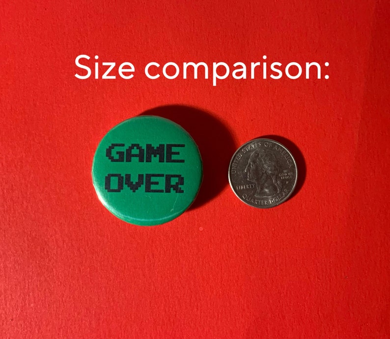 May include: Green button with the text "GAME OVER" in black pixelated letters. The button is about the size of a US quarter.