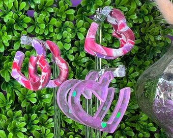 Op de afbeelding: Drie paar hartvormige creolen op displays. De oorbellen zijn gemaakt van hars en hebben een roze en wit swirl-patroon.