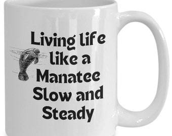 May include: White ceramic coffee mug with a black illustration of a manatee swimming and the text "Living life like a Manatee Slow and Steady".