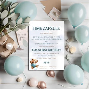 以下が含まれることがあります： タイムカプセルと「KOA's First Birthday」の文字が書かれた青と白のファーストバースデーの招待状。招待状にはテディベアの絵と、日付、時間、場所などのパーティーの詳細が記載されています。