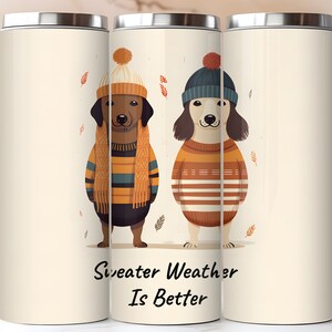 May include: Two dogs wearing sweaters and hats stand against a white background with the text "Sweater Weather Is Better". The dogs are brown and white with orange and brown sweaters. The background has a subtle pattern of falling leaves.