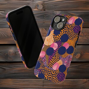 May include: A phone case with a colourful abstract design featuring orange, pink, blue and white circles and dots on a navy blue background.
