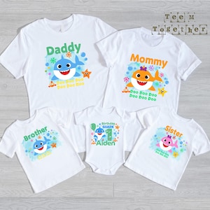 May include: A set of five white t-shirts and one white baby bodysuit featuring colorful cartoon shark graphics. The designs include the text Daddy, Mommy, Brother, Sister, and Birthday Shark 1 Aiden, accompanied by bubbles and stars.