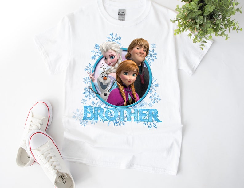 May include: White t-shirt with a blue, white, and pink graphic of Elsa, Anna, and Olaf from the movie Frozen. The graphic is in a circle with the word "BROTHER" below it.