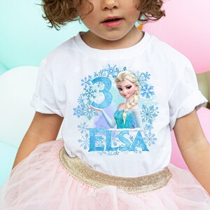 May include: White t-shirt with a blue and white graphic of Elsa from Frozen. The graphic includes a blue number 3 and the word "Elsa".