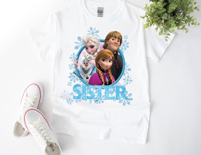 May include: White t-shirt with a graphic of Elsa, Anna, and Olaf from the movie Frozen. The graphic is surrounded by snowflakes and the word "Sister" is printed below the graphic.