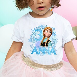 May include: White t-shirt with a blue and white snowflake design, a picture of Anna from Frozen, and the number 3. The text "ANNA" is printed below the image.
