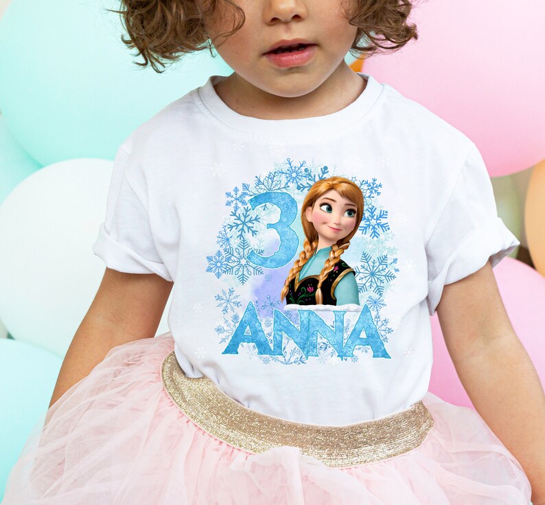 May include: White t-shirt with a blue and white snowflake design, a picture of Anna from Frozen, and the number 3. The text "ANNA" is printed below the image.