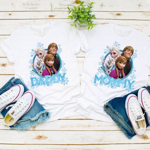 May include: Two white t-shirts with a Frozen theme. The left shirt says "Daddy" and the right shirt says "Mommy". Both shirts feature a graphic of Anna, Elsa, Olaf, and Kristoff.