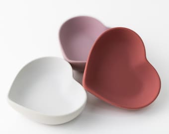 May include: Three heart-shaped ceramic dishes in white, pink, and red.