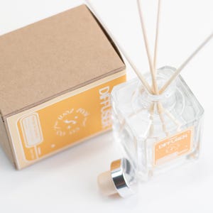 May include: A clear glass diffuser bottle with wooden reeds, a silver-capped cork, and a matching box. The box and bottle have orange labels with the word "Diffuser". The product is designed for home fragrance.