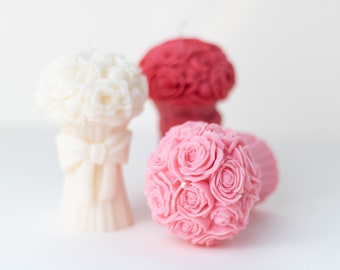 May include: Three decorative flower bouquet candles. One is white, one is pink, and one is red.