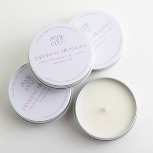 May include: Three silver tins of soy wax candles with the label "Zenit Co." and the scent "Japanese Blossom: Cherry Blossom, Rose, Orange, Sandalwood". The candles are hand-poured and 100% natural.