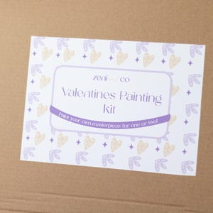 May include: A white box with a purple and yellow design. The box says "Zeni & Co Valentines Painting Kit" and "Paint your own masterpiece for one or two!"