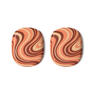 May include: A pair of oval-shaped objects featuring a repeating pattern of swirling, wavy lines in shades of dark brown, terracotta orange, and light cream. The surface of each oval is smooth and glossy, displaying a consistent, fluid, and abstract design.