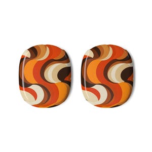 May include: Two oval-shaped decorative items featuring a repeating pattern of curved, overlapping bands in shades of orange, dark brown, cream, and tan. The design consists of smooth, flowing lines that create a layered, abstract visual effect.