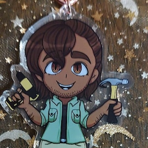 May include: Acrylic charm featuring a cartoon character holding a hammer and a drill, with a beer mug charm below. The character wears a green shirt and khaki pants. The charms are connected by a rose gold clasp.