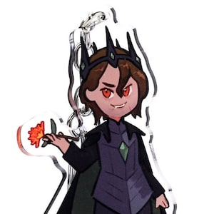 May include: A clear acrylic keychain featuring a cartoon illustration of a character in dark attire, a crown, and a flower. The character has red eyes and a stern expression. The keychain has a silver metal ring.