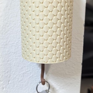 May include: A white ceramic planter with a textured pattern holds a green and white cactus with a pink flower. A set of keys hangs from a hook attached to the planter.