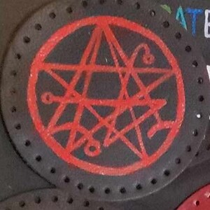 May include: A red pentagram drawn on a black background. The pentagram is surrounded by a red circle. The background is a black leather surface with small holes.