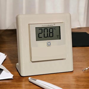 Puede incluir: Un termostato homematic® blanco con una pantalla digital que muestra 20,8 grados Celsius. El termostato tiene un botón y un símbolo inalámbrico.