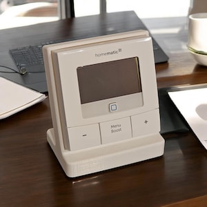 Könnte beinhalten: Weißer homematic® Thermostat mit digitalem Display, Menü- und Boost-Tasten sowie Plus- und Minustasten.
