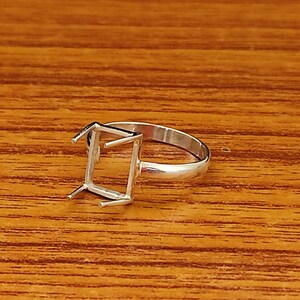 Op de afbeelding: Een zilveren ring met een vierkante bezel-setting. De ring is ontworpen om een ​​edelsteen of ander decoratief element vast te houden.
