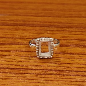 Op de afbeelding: Een zilveren ring met een rechthoekige bezel-setting. De bezel is versierd met kleine kralen rond de rand.