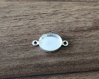 May include: A silver-colored oval bezel connector with two small loops on either side. The bezel has a shallow, concave surface. The connector is designed for jewelry making and crafting.
