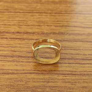 May include: A gold-toned ring with an oval-shaped bezel. The ring is designed to hold a stone or other embellishment.