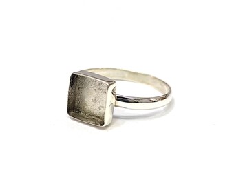 Puede incluir: Un anillo de plata con un engaste cuadrado. El anillo está diseñado para sujetar una piedra o cabujón de forma cuadrada.