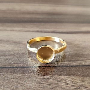 Puede incluir: Un anillo de oro con un bisel redondo vacío. El anillo está hecho de metal texturizado y tiene un diseño simple.