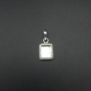 May include: A silver-colored pendant with a rectangular frame and a decorative rope-like border. The pendant has a small loop at the top for a chain. The center is open, ready for a stone or other embellishment.