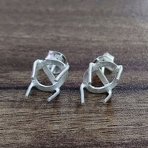 Op de afbeelding: Twee zilveren oorbelbevestigingen met een ronde bezel en vier grijpklauwen. De bevestigingen zijn ontworpen om een ​​edelsteen of andere versiering vast te houden.