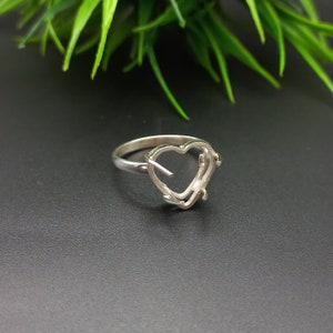 May include: A silver ring with a heart-shaped setting. The ring is designed to hold a stone or other embellishment.
