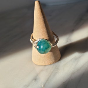Puede incluir: Un anillo de alambre plateado con una piedra de ágata verde.