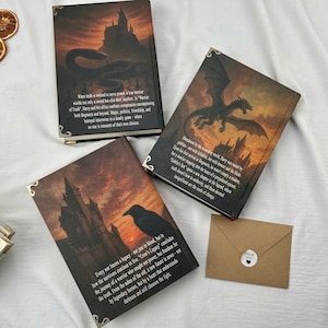 Pu&ograve; includere: Tre libri con copertina rigida a tema fantasy con illustrazioni di un serpente, un drago e un corvo, ognuno con testo. I libri hanno protezioni angolari decorative. &Egrave; presente anche una piccola busta marrone con un adesivo "grazie".