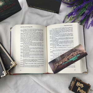 May include: An open book with gold-edged pages, displaying text from "James Potter and the Morrigon Web." A bookmark with the title is visible. Other books and a small "Harry Potter" music box are also present.