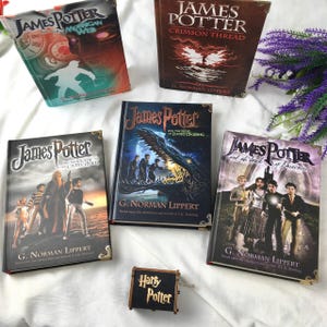 May include: Five "James Potter" books by G. Norman Lippert are displayed, each with unique cover art and titles. A small wooden music box with "Harry Potter" text is also present. The books are hardback.