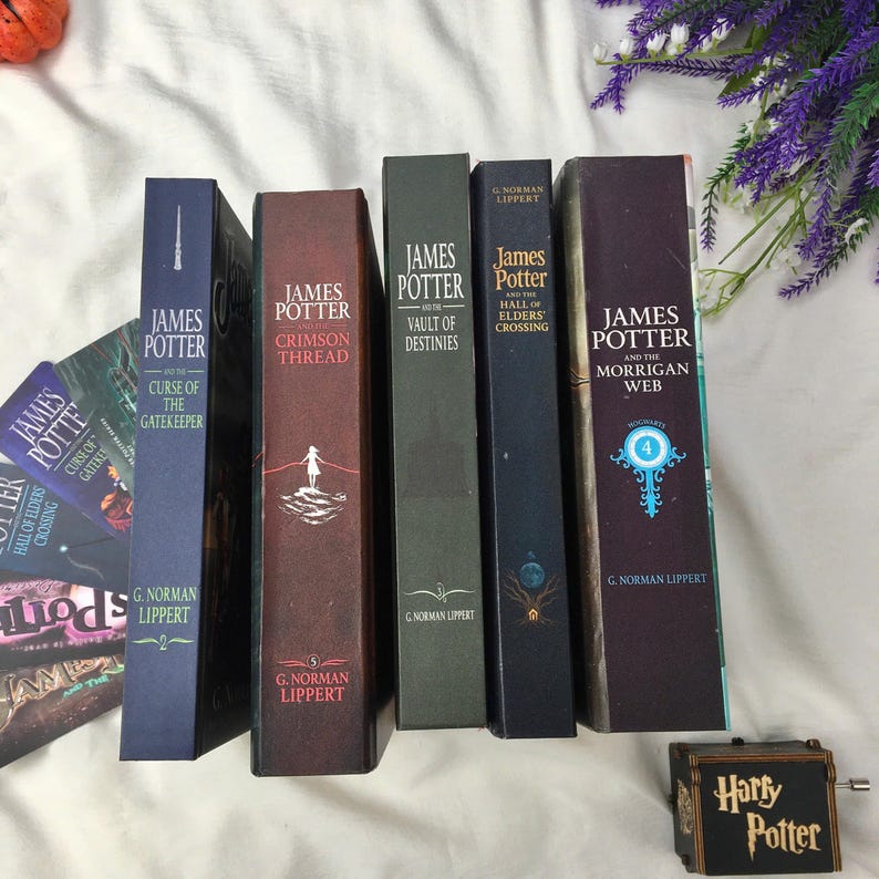 May include: A selection of hardcover books, including titles such as "James Potter and the Hall of Elders Crossing" and "James Potter and the Morrigan Web." The books are in shades of blue, burgundy, and green. A small "Harry Potter" music box is also visible.