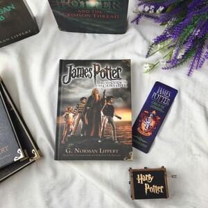 May include: An assortment of Harry Potter-themed items, including books and accessories. The main book, "James Potter and the Curse of the Gatekeeper," has a cover illustration of characters. A bookmark and a music box with "Harry Potter" text are also present.