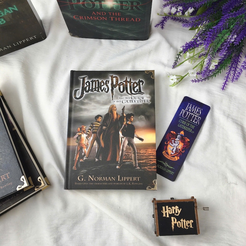 May include: An assortment of Harry Potter-themed items, including books and accessories. The main book, "James Potter and the Curse of the Gatekeeper," has a cover illustration of characters. A bookmark and a music box with "Harry Potter" text are also present.